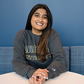 Vaibhavi Bharadwaj sits at a table against a dark blue background, smiling at camera